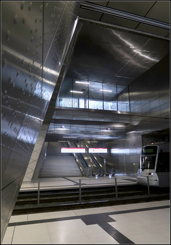 Rechtwinklig zur Benrather Straße -

Am nördlichen Ende der U-Station Benrather Straße kreuzt diese Straße im rechten Winkel die Bahnstrecke. In diesem Bereich sind auch die Zugangstreppen angeordnet und diese liegen jeweils in Richtung der Benrather Straße und führen deshalb direkt auf die Gleise zu. Der Hallenbereich ist an dieser Station kürzer gehalten, aber auch hier besteht eine Verbindung zum Tageslicht. Aufzüge wurde an den südlichen Bahnsteigenden angeordnet und führen in die Kasernenstraße.

Düsseldorf, Wehrhahnlinie, 14.08.2018 (M)