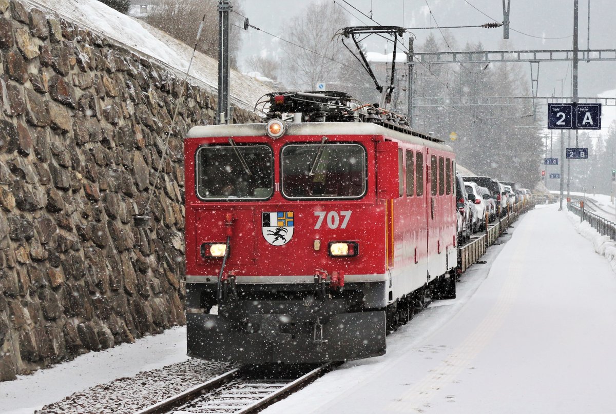 RhB Ge 6/6 II Nr. 707  Scuol  bei einem Halt auf einem Gegenzug (IR 1121) mit einem Neuwagen-Autozug im Bahnhof Tiefencastel.

Aufgenommen am 21. Februar 2018 aus dem  Gegenzug  IR 1121 von Chur - St. Moritz.