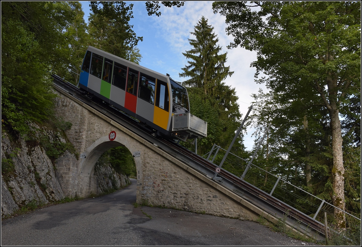 Standseilbahn auf den Mont Soleil. Hier ist alles irgendwie steil und schief. Ausser der kleinen Strasse, die ganz offensichtlich die Autofahrer zum Rasen verleitet, wenn denn das Auto mal auf Touren gekommen ist. Zwar war die Sonne schon hinter dem Steilhang verschwunden, aber doch bietet das kleine Bähnchen einen bunten Reiz. Saint-Imier, Juli 2017.