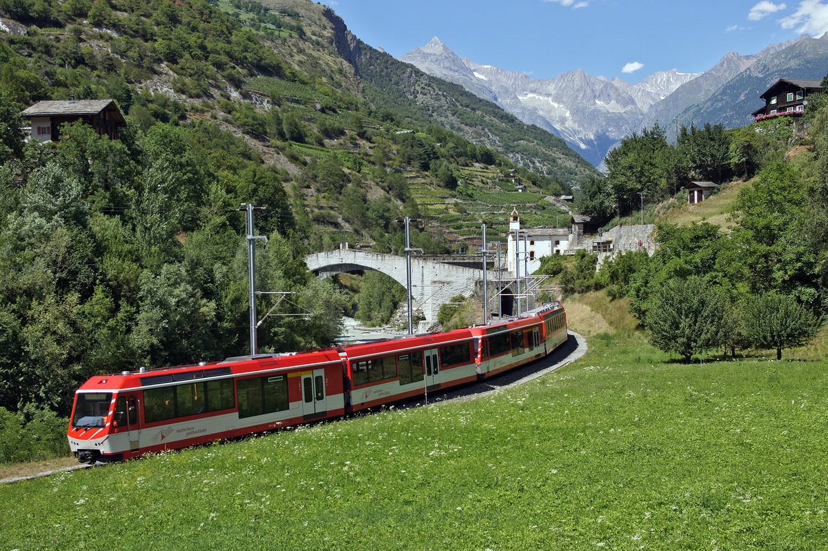 Triebzug der Matterhorn-Gotthard-Bahn am 06.07.2017 an der alten Steinbrücke bei Stalden im Vispertal (Kanton Wallis).