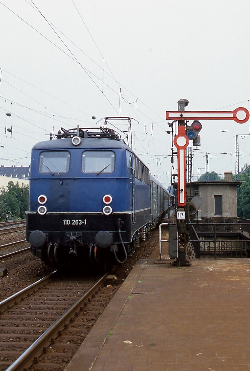 Um 1980 fährt 110 263-1 mit einem Eilzug in den Bahnhof Düsseldorf-Bilk ein. Im Zusammenhang mit dem Bau der Ost-West-S-Bahn wurden der Bahnhof und die Brücke, über die der Zug gerade fährt, umgebaut. Dabei verschwand leider auch das schöne Ausfahrtsignal.