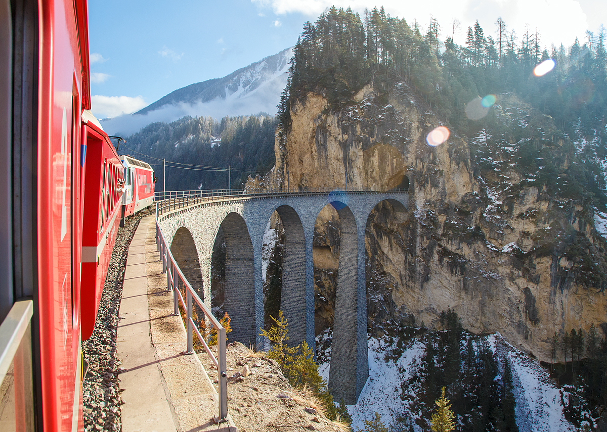 
UNESCO-Weltkulturerbe Albulabahn: Gezogen von der RhB Ge 4/4 III 651, fahren wir am 18.02.2017 mit dem RE (Chur -  St. Moritz) der Rhätischen Bahn (RhB), über den berühmten, 136 m langen und 65 m hohen, Landwasserviadukt bei Filisur, danach geht es direkt in den 216 m langen Landwassertunnel.
