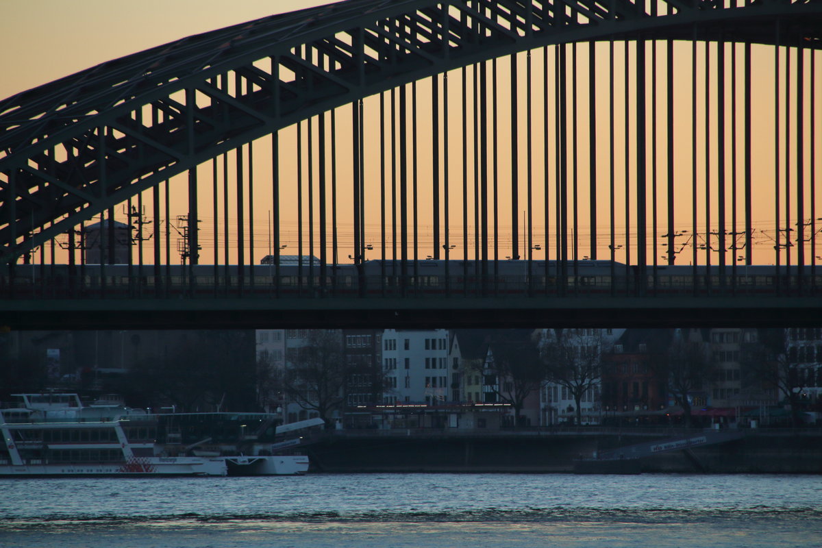 Während oben noch die warmen Farben der Sonne das Bild ausmachen, liegen die Häuser und der Rhein schon im kalten Schatten.
Gerade passiert ein ICE 1, den man an dem charakteristischen „Buckel“ des Speisewagens erkennen kann, als ICE 1026 (Frankfurt(Main)Hbf - Hamburg Altona) die Hohenzollernbrücke.

Hohenzollernbrücke, 25. November 2016