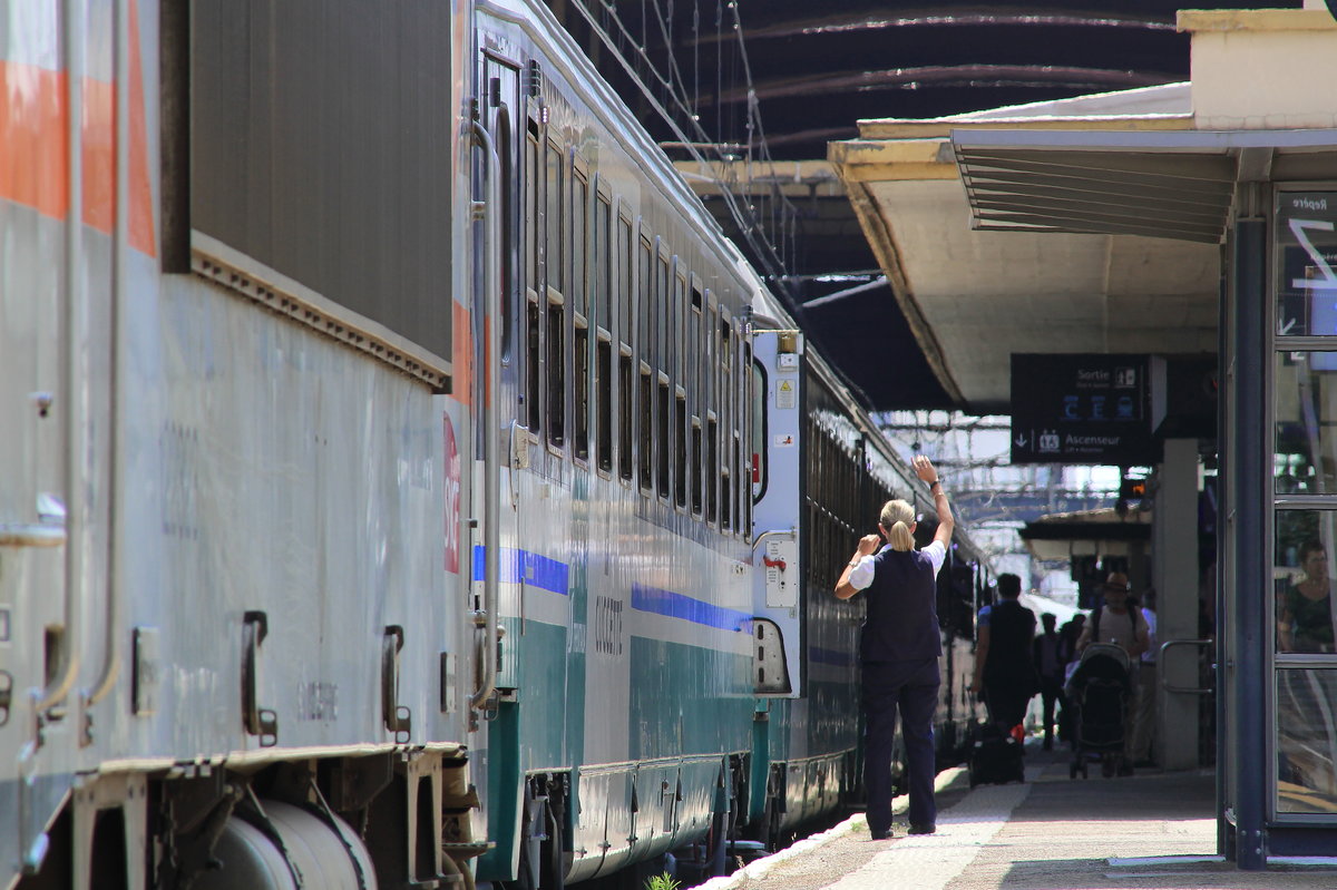 Zug kommt an, Schaffnerin steigt aus und gibt einem anderen Mitarbeiter ein Signal. So gesehen im Bahnhof von Nimes.
Nimes, 11. Juli 2016
