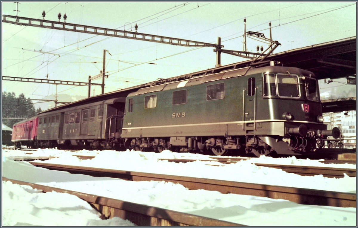 Die SMB* Re 4/4 III N° 181 wartet mit ihrem Regionalzug besthend aus EBT-ABDi und EBT/SMB/VHB B nach Solothurn in Zugausgangsstation  Moutier auf die Abfahrt. 

(Gescanntes Foto)
23. Februar 1985.

*SMB: Solothurn - Münster (Moutier) Bahn, später RM, nun BLS.