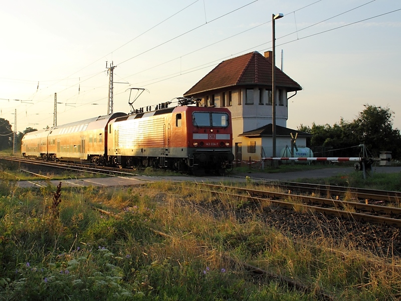 143 034-7 mit RB 26854 nach Nordhausen wird am 4. August 2009 in Wallhausen von der aufgehenden Sonne beschienen. Wegen Bauarbeiten fhrt der Zug auf dem Gegengleis.