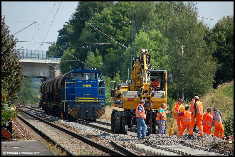 Am Sonntagmorgen des 27.07.08 wird bei den Gleisbauarbeiten zwischen Aalen und Goldshfe feste gewerkelt. Am Hp Hofen(b Aalen) arbeitet der Bautrupp samt Zweiwegebagger, dahinter steht V 2104 der MWB mit einem kurzen Schotterzug.