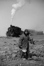 Arbeiter und im Hintergrund eine Lok der Baureihe Sy ( Hohes Ziel ) auf einer Abraumhalde nahe der Industriestadt Fuxin (province Liaoning).

China, April 2013 