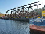  Friedhofsbahnbrücke  (ehemals den Teltowkanal überbrückend) im Vordergrund, teils zerschnitten auf einem Lastschiff. Die 105 Jahre alte Brücke verband Kleinmachnow und Stahnsdorf im Süden Berlins. Die 200 Tonnen schwere Fachwerkkonstruktion wurde 2018 abgerissen. Sie war Teil einer ca.4km langen Eisenbahnverbindung von Wannsee zu einem der größten deutschen Friedhöfe in Deutschland, dem in Stahnsdorf. Foto: Herbst 2018 