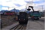 Während 01 1533-7 mit einem LKW bekohlt wird, rauscht im Hintergrund ein Taurus der ÖBB vorbei.