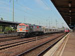 hvle Tiger V330.8 (250 009-8) fährt am frühen Abend mit einem langen Schüttgutwagenzug (Kies) durch den Bahnhof Berlin Schönefeld Flughafen am 15.