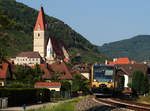 Das Bild zeigt die Wachaubahn Regiosprinter (Baureihe 654) mit dem Zug nach Emmersdorf in der Nähe der Kirche von Weissenkirchen.