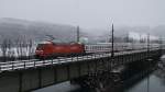 Bei dichtem Schneetreiben ist 101 121-2 am 26.1.2014 mit dem IC 1284 ``Großglockner`` von Schwarzach St. Veit nach Flensburg unterwegs. Hier passiert der IC die Innbrücke bei Kirchbichl Richtung Kufstein. Bis Wörgl hat eine 1116 der ÖBB den Zug gezogen und dann war Lok- und Richtungswechsel.