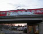 Ein Kurzzug der S2 nach Dietzenbach huscht hinter dem Transparent mit der selbsterklrenden Ankndigung am 12.03.2006 ber die Bahnunterfhrung in Frankfurt am Main-Zeilsheim.