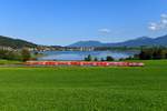 Bei Reinertshof ergibt sich dieser Blick auf den Hopfensee und die Ortschaft Hopfen am See. 218 414 schob am 20. September den RE 57513 nach München HBF. Die Reisenden hatten an diesem schönen Tag sicherlich eine angenehme Fahrt in den Doppelstockwagen. Im Hintergrund erkennt man das Ammergebirge. 