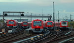 In der Abenddämmerung sind drei S-Bahn-Züge der Baureihe 474 und ein Zug der Baureihe 472/473 im Gleisvorfeld des Bahnhofes Hamburg-Altona abgestellt, rechts fährt ein 474 in Richtung