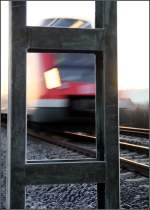 Kalter Dezembermorgen -    Die Kanten des Oberleitungsmasten werden vom Raureif nachgezeichnet, während auf den Gleisen ein moderner S-Bahnzug vorbei rauscht.