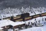 Bahnhof Brocken am Nachmittag des 26.01.2013. Diese Aufnahme erfolgte per Zoom durch die Scheibe von der Aussichtsplattform des Brockenturms aus. Der vordere Zug (auf Gleis 1) ist Planzug P8922, welcher gleich nach Drei Annen Hohne fahren wird. Direkt dahinter, auf Gleis 3, steht  Sonderzug  Quedlinburger Brockenexpress  mit Zuglok 99 7245 bereit, der einige Zeit spter nach Wernigerode startet. Von dem Kleinbus am Bahnhof sollte man sich nicht tuschen lassen. Dieser gehrt dem Brockenwirt. Es ist nur einigen wenigen Fahrzeugen mit Sondergenehmigung gestattet, auf den Brocken zu fahren! Der ffentliche Verkehr endet in Schierke. Sptestens hier mu man seinen Privat-PKW abstellen und den Rest der Strecke zu Fu, oder mit einem Zug der HSB bewltigen.