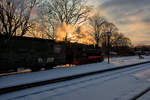 Der RASENDE ROLAND mit der Lok 994632 fährt im abendlichen Gegenlicht an den verschneiten Bahnsteig des Bahnhofs Binz LB.