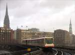 Whrend ein Regenschauer abzieht, strebt ein Zug der Hochbahn U-Bahn Linie U3 Mmmelmannsberg - Barmbek der Station Baumwall entgegen; Hamburg, 4.12.2007  