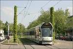 Mit der Straßenbahn in den Freiburger Westen -    Zwischen zwei grünen Masten hindurch verlässt eine Combino-Straßenbahn im Stadtteil Betzenhausen die Haltestelle 'Am
