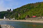 Das wechselhafte Wetter am 27. April 2017 wurde zur Erkundung der Gegend rund um St. Goarshausen genutzt. So wanderte ich auch zur Loreley Statue, die sich auf einer Landzunge befindet, die den Rhein von einem kleinen Binnenhafen abtrennt. Hier hat man einen schönen Blick auf den Ort und die Burg Katz. Auch erkennbar ist der sogenannte Häusener Kran. Der 1917 erbaute Kran diente bei Niedrigwasser dem Leichtern der Schiffe. Außerdem wurden mit dem um 360 Grad drehbaren Arm, der bis zu acht Tonnen tragen konnte, Güter wie Steine, Koks, Sand und Getreide zwischen der Rheinschifffahrt und der nassauischen Kleinbahn umgeladen. Glücklicherweise gab es ein kleines Wolkenloch, als 187 107 mit ihrem EZ 51456 von Gremberg Gsf nach Mannheim Rbf diese auch noch durch eine Entenkolonie bereicherte Szenerie passierte.