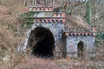 Das Nordportal des Gensbergtunnels an der ehemaligen Weiltalbahn, kurz vor der Einfahrt in den Bahnhof Weilburg. Am 18.03.2006 hat die Vegetation die Sicht noch nicht komplett versperrt. Seit September 1969 gab es hier keinen planmäßigen Personenverkehr mehr, der Güterverkehr wurde, zumindest sporadisch, bis Anfang 1988 aufrecht erhalten. Das kleine Häuschen neben dem nicht zugemauerten Tunnel diente übrigens als Wärterbude.