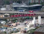 Die DLR in ungeordnetem Umfeld -    Ein Zug der Londoner DLR auf der Fahrt nach Woolwich Arsenal zwischen den Stationen Canning Town und West Silvertown.