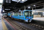 Die IR Ishikawa Privatbahn: Als am 14.März 2015 der Hochgeschwindigkeitszug Shinkansen von Tokyo her via Nagano und Toyama die Stadt Kanazawa am Japanischen Meer erreichte, wurde die bisherige Hauptstrecke von verschiedenen privaten und lokalen Betreibern übernommen. Innerhalb der Praefektur Ishikawa (mit Hauptstadt Kanazawa) entstand so die IR Ishikawa Bahn, die - in Verbindung mit der Ainokaze Toyama Bahn in der Praefektur Toyama - die lokalen Dienste im Raum Toyama und Kanazawa erbringt. Von den JR West Japan wurden dafür 5 Züge Serie 521 übernommen. Der Name der Bahn kann englisch «Ishikawa Railway» verstanden werden, oder als «ai aru»-Bahn, also eine Bahn, die liebevoll ist, oder als «ein Buchstabe vor J, nämlich I – also eine Stufe besser als JR». Die Farbgebung der Züge ist das charakteristische blau der alten Seidenstoff-Färbetradition von Kanazawa.Im Bild steht Zweiwagenzug 521-10 im Bahnhof Kanazawa, 19.März 2024 