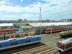 Auf der Fahrt im Zug des Hanshin-Konzern kommt man auch am Betriebswerk Amagasaki vorbei, in dem Hanshin Expresszüge (beige/orange und silbrig mit orangen Türen), Hanshin Lokalzüge (hell- bzw. dunkelblau) und ein Zug des Kintetsu-Konzerns stehen, der aus der Stadt Nara im Osten von Ôsaka gekommen ist. 22.März 2014. 