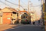 Wie in den 50er Jahren sieht es im Dörfchen Asakura bei Kôchi im Süden der Insel Shikoku aus. Der alte Strassenbahnwagen 213 hält bei einer Ausweiche auf einer Einspurstrecke, um aussteigen zu lassen, eine Frau hat ihren Schirm fallen lassen, der vom Schaffner aufgehoben wird. 5.November 2017. 