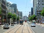 Die Strassenbahn von Nagasaki - die Innenstadt jetzt: Wuchtige moderne Bauten haben hier das alte Chaos verdrängt, doch wie durch ein Wunder ist die Strassenbahn noch da. Der  alte Wagen 364, der meinem Wagen folgt (Bild nach hinten aufgenommen), ist noch eine echte Rumpelkiste, wogegen ein moderner Gelenkwagen (Wagen 3002) gerade gekreuzt hat. 8.August 2013.  