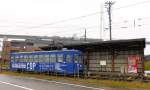 Takaoka Manyô-Linie, alte Wagen Serie 7070: Wagen 7076 am 25.Oktober 2013 an der Endstation Koshinokata. Rechts vom Wagen ist die Tafel mit einem rund 1230 Jahre alten Gedicht aus der Manyô-Sammlung zu sehen, mit welchem der damalige örtliche Verwalter eine Nachricht an seine Geliebte in der Hauptstadt schickt; es lautet etwa so:  Im stürmischen Ostwind hier, an der Küste wo ich einsam lebe, wälzt sich heran Welle um Welle: sich vielfach türmend, so wie meine Sehnsucht nach dir  