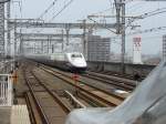 Whrend im Vordergrund die Schnauze eines haltenden Shinkansen zu sehen ist, braust ein anderer Zug mit Hchstgeschwindigkeit (>300km/h) durch den Bahnhof Oyama - 28/06/2007