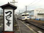 Serie 411/415: Zug mit Steuerwagen KUHA 411-206 lehnt sich bei der Einfahrt in Kiyama in die Kurve. Auf dem Bahnsteig steht ein grosser  Werbekasten  mit der Aufschrift:  (Besucht den) für seine Azaleen berühmten Tempel Daikôsenji . 28.November 2010.
