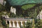 Hoch über dem Talboden fährt die 1042.14 mit einem Schnellzug in die 1970ern über das bekannte Krauselklause Viadukt den Semmering talwärts kurz vor Breitenstein.
Das Bild entstand auf der Modellbahn des GEMEC in Graz am 8.12.2023.
