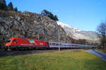 Während die leicht angezuckerten Berge noch im vollen Sonnenschein liegen, zieht 1216 015-8 mit der Italien-Flagge ihren EC 87  DB-ÖBB EuroCity  (München Hbf - Venezia Santa Lucia) vor der Kulisse der Wiesinger Steinwand Richtung Jenbach, 08.12.2018.