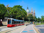 Wien. Flexity 318 ist hier am 12.08.2023 als Linie 6 kurz vor der Haltestelle Gumpendorfer Straße zu sehen. Im Hintergrund sieht man die Kirche Maria vom Siege.