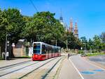 Wien. Flexity 347 ist hier am 12.08.2023 als Linie 18 kurz vor der Haltestelle Gumpendorfer Straße zu sehen. Im Hintergrund sieht man die Kirche Maria vom Siege.