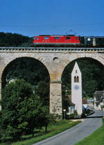 SBB: Nicht erkennbare Re 4/4 II mit Viadukt und Kirche von Rümlingen im Mai 1994.