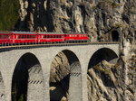 rot in grau.
Ge 6/6 II 707  Scuol  zieht den RE 1153 (Chur - St.Moritz) über das Landwasserviadukt. Seit 2008 gehört es als Teil der Albulastrecke zum Unesco Weltkulturerbe in der Landaschaft Albula und Bernina. 
(05. Mai 2016)