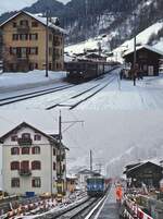 Der Bahnhof Klosters Dorf im Februar 1981 und am 01.04.2022: Auf der oberen Aufnahme kommt die Ge 6/6 II 704 mit einem Zug aus Landquart an, darunter durchfährt die Ge 4/4 II 619 den Bahnhof mit einem RE nach Scuol-Tarasp. Im Zuge des momentan laufenden Umbaus wird der Bahnhof neue Hochbahnsteige erhalten, deren Länge auch für die geplanten Flügelzüge ausreicht. Außerdem wird die Strecke von Klosters Dorf nach Klosters Platz doppelspurig ausgebaut.