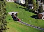 Regionalzug von Arosa nach Chur verlässt soeben den Tunnel beim Bahnhof Arosa und fährt talwärts Richtung Chur. An 2. Stelle verkehrt der Bärenwagen: eine Attraktion für die Kinder mit Bücher, Bilder und Wettbewerb. Das Bild wurde vom Balkon einer Ferienwohnung aufgenommen. Arosa, 10.10.2023