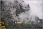 Der verspätete Glacier Express 905 taucht aus einer tiefhängenden Wolke auf oberhalb von Filisur.