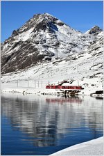 Dienstzug mit ABe 8/12 3514 am Ufer des schwarz gefrorenen Lago Bianco mit dem Piz Albris im Hintergrund.