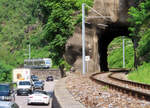 Viel Verkehr auf der Hauptstrasse, währenddem der Regionalzug von Camedo nach Locarno in wenigen Sekunden den kurzen Tunnel zwischen Ponte Brolla und Solduno S. Martino durchfährt. Locarno, 29.7.2023