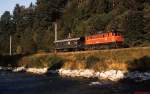 Mit einem Güterzugbegleitwagen ist eine 1245 an einem Augustmorgen 1989 am Ennsufer in Schladming unterwegs