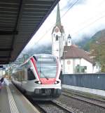 rabe-523-flirt rund und spitzig: Seit die NPZ weitgehend in Fl�elen verschwunden sind, ist die Kirche dort wieder das eckig- und spitzigste Element beim Bahnhof Fl�elen. Am 09.10.09 begegnet sie dem RABe 523 018.