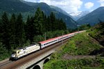 Durch den Wald zwischen Bad Gastein und Anger rauscht am 13. Juli 2013 die ungarische 470 010 mit ihrem OIC 691 auf der Rückfahrt nach Salzburg. An dieser Stelle blickt man auf Hüttenkogel und Ankogel, sowie den Reichebenwald.