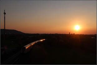 Der Sonne entgegen -    Abendhimmel mit tiefstehender Sonne, eine Landschaft ins Dunkel gehüllt und ein IC2-Zug als dickes Glühwürmchen.